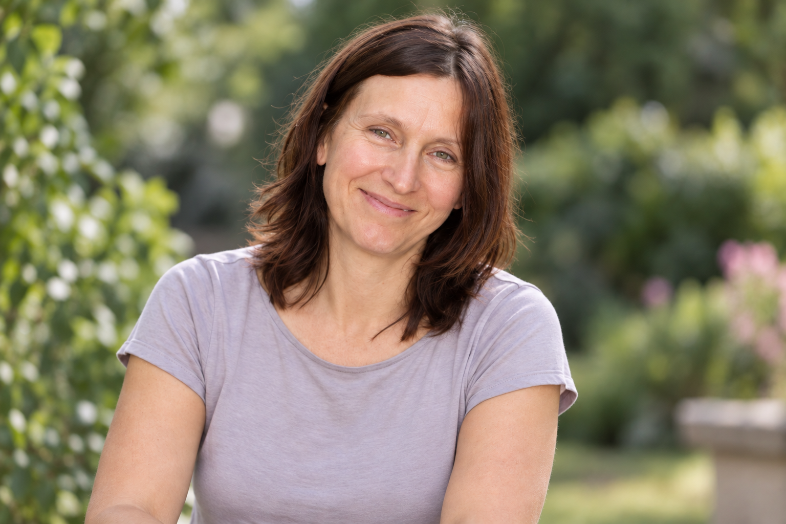 Sabine Hellmich lächelt in die Kamera, im Hintergrund ein grüner Garten.